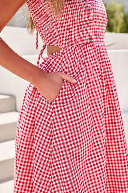 Woman wearing the Gingham Open Back Midi Dress in red, standing outdoors with her hand in a pocket near steps.