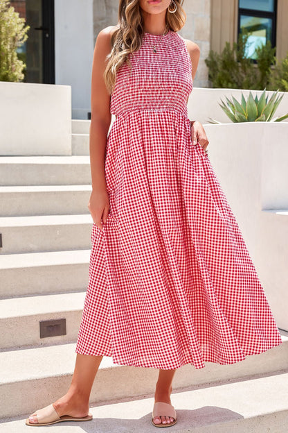 Woman in the Gingham Open Back Midi Dress - Red stands outdoors in sandals, her wavy hair flowing in the breeze.