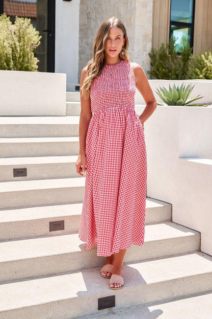 Woman wears the Gingham Open Back Midi Dress - Red, standing outdoors on steps with plants and a modern building behind her.