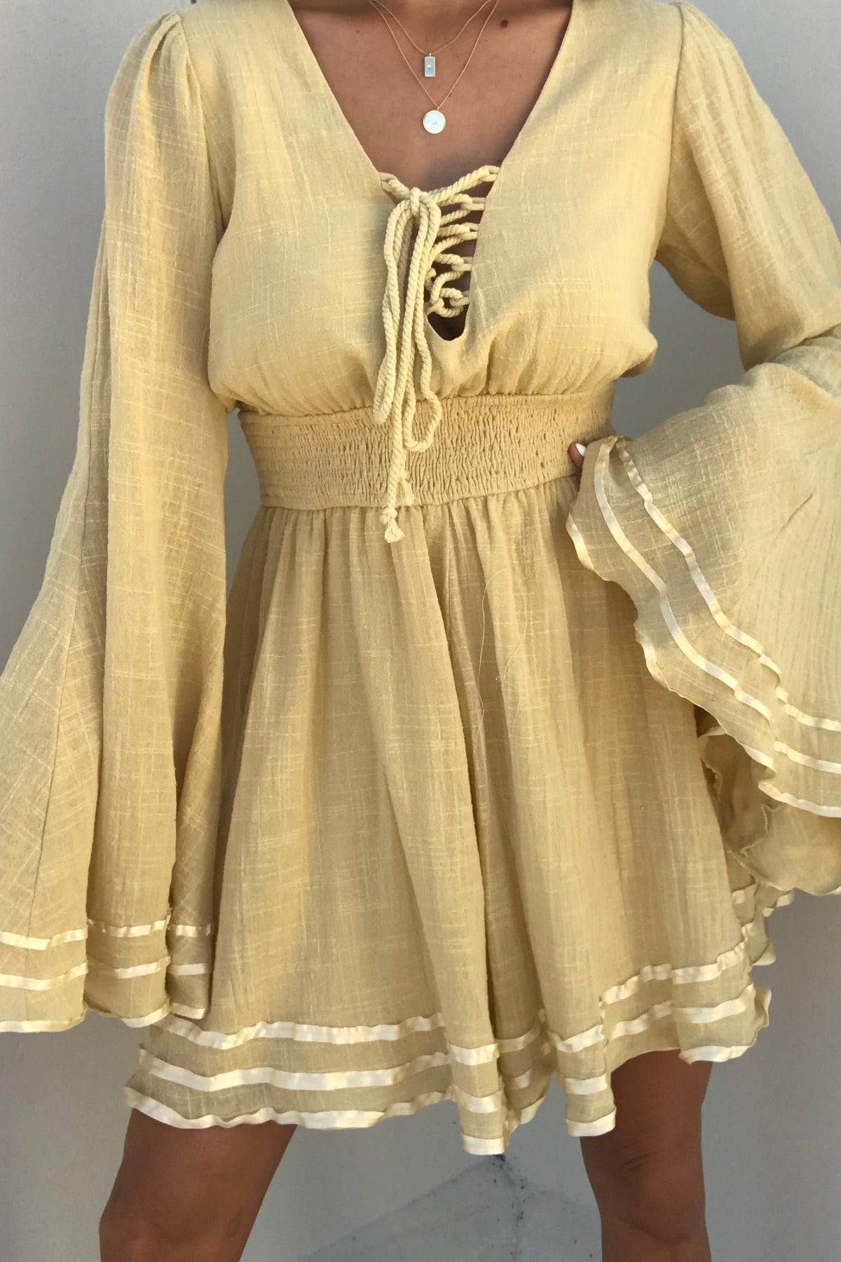 Woman in a Golden Hour Bell Sleeve Romper - FINAL SALE, featuring flared sleeves, lace-up front, smocked waist, and white trim.