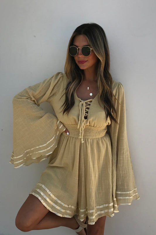 Woman in sunglasses wears the Golden Hour Bell Sleeve Romper - FINAL SALE, standing against a plain white wall.