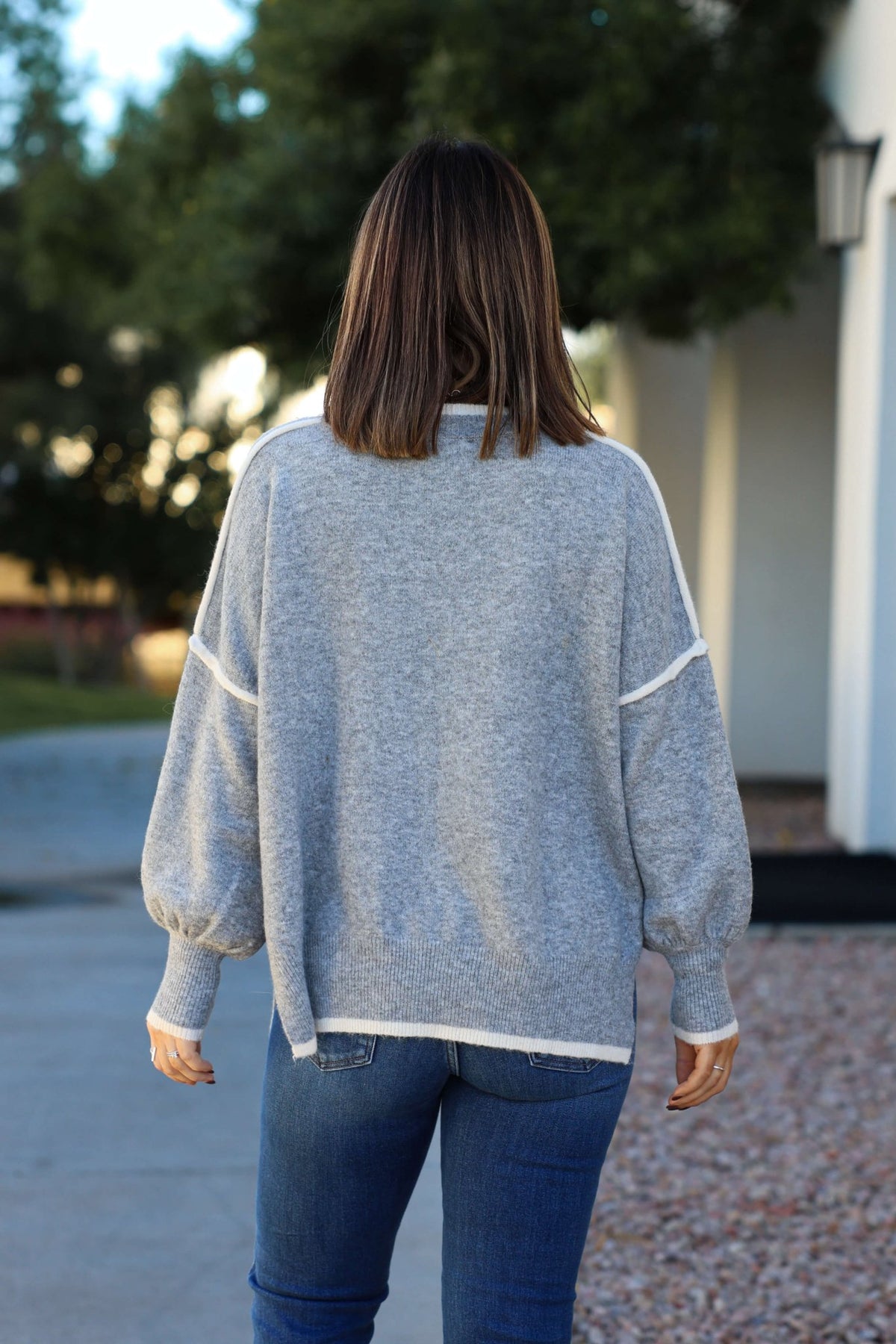 Wearing the Grey Contrast Detail Pullover Sweater, a person in jeans enjoys fall outdoors, facing away in cozy style.