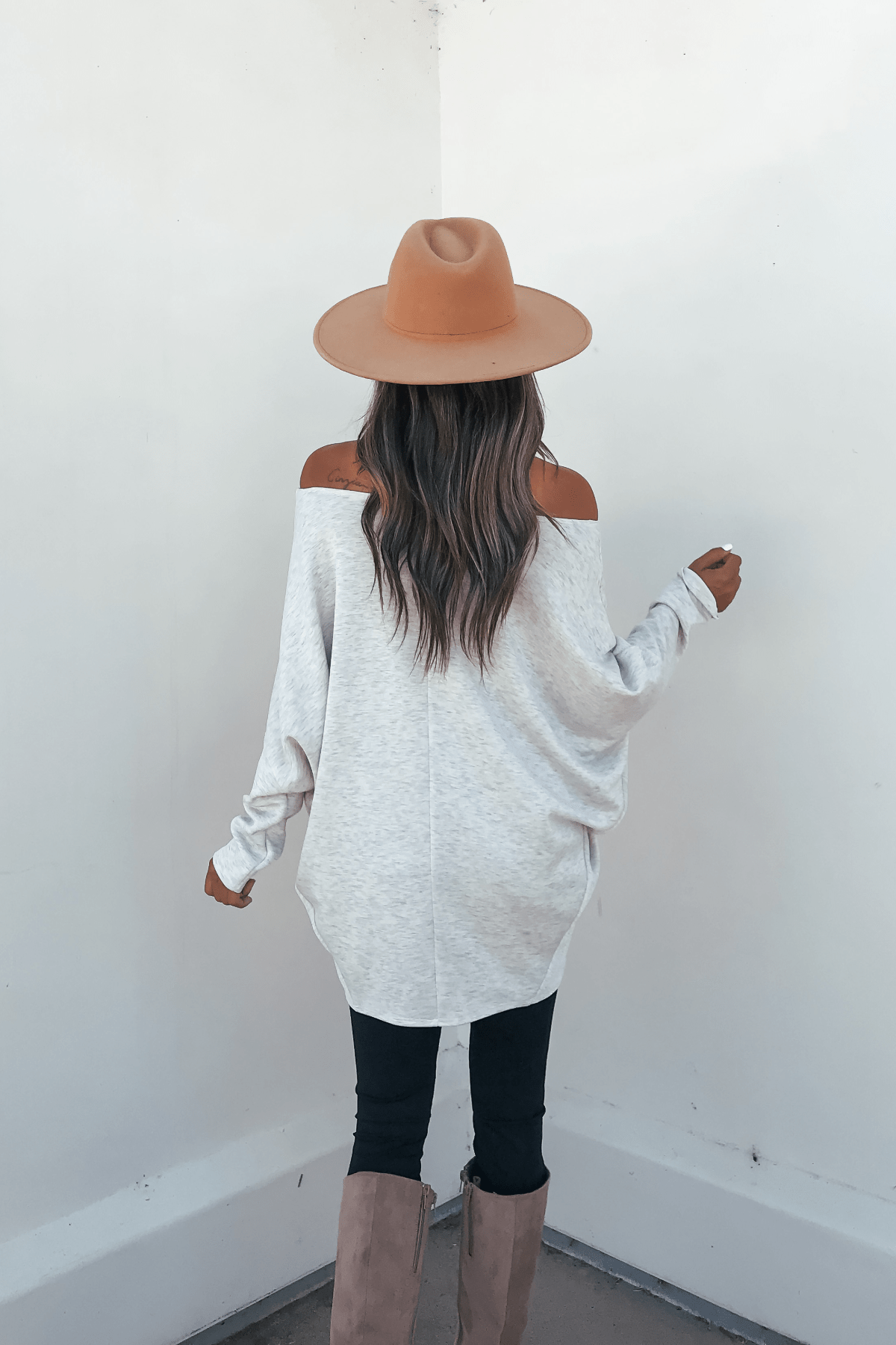 A woman in a tan hat, black pants, and tan boots wears the Grey Soft Cloud Scuba Pullover with a relaxed silhouette, facing away.