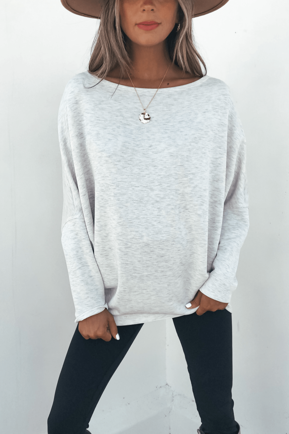 Woman in a wide-brim hat and Grey Soft Cloud Scuba Pullover poses stylishly against a white wall.