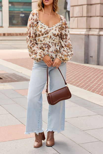 Woman in a Hazel Floral Print Top - Cream, light jeans, brown boots, and handbag stands on a city sidewalk.