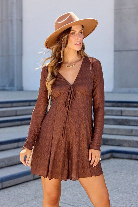 Woman in a brown Lace Tie Romper stands outdoors near steps, looking to the side, wearing a tan wide-brim hat.