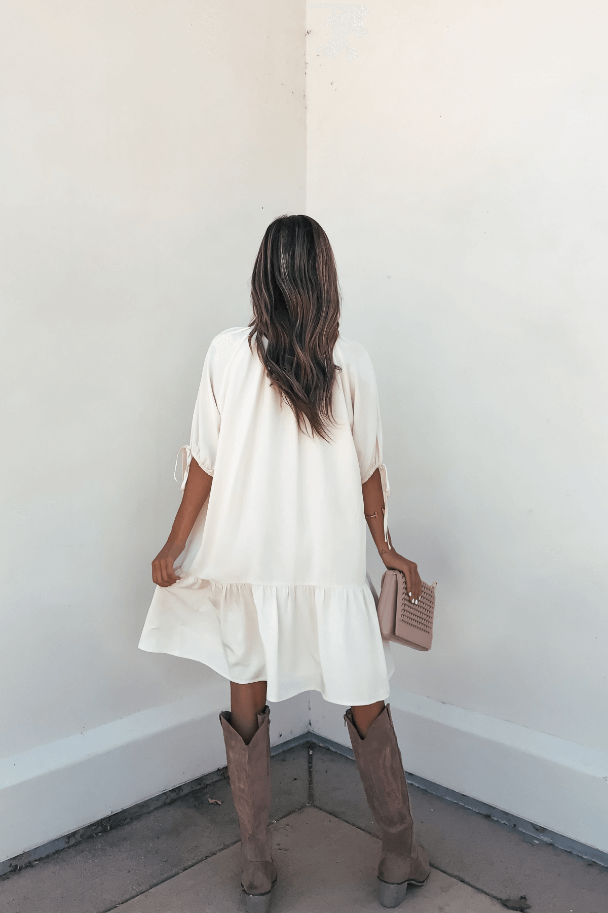 Woman in a Laurie Cream Button Down Mini Dress-FINAL SALE and brown boots holds a beige studded clutch, facing the corner.