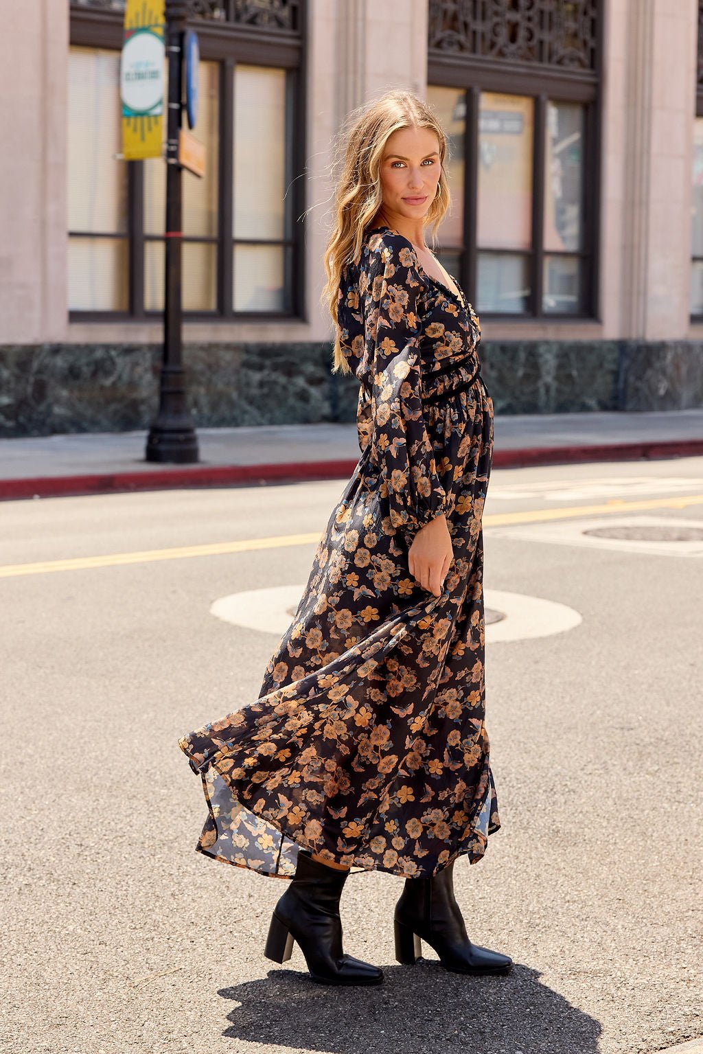 Woman in the Maple Floral Maxi Dress - Black with black boots, stands on a city street, her dress flowing gracefully in the breeze.