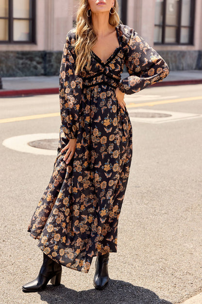 Woman in the Maple Floral Maxi Dress - Black and boots stands on a city street, hand on her hip.