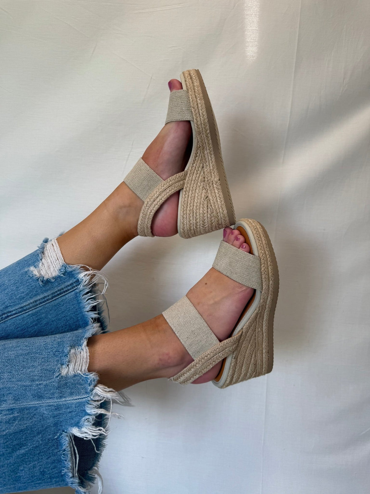 Model wears MIA Brittni Natural Wedge Espadrille Sandals with frayed blue jeans, feet up against a plain light background. FINAL SALE.