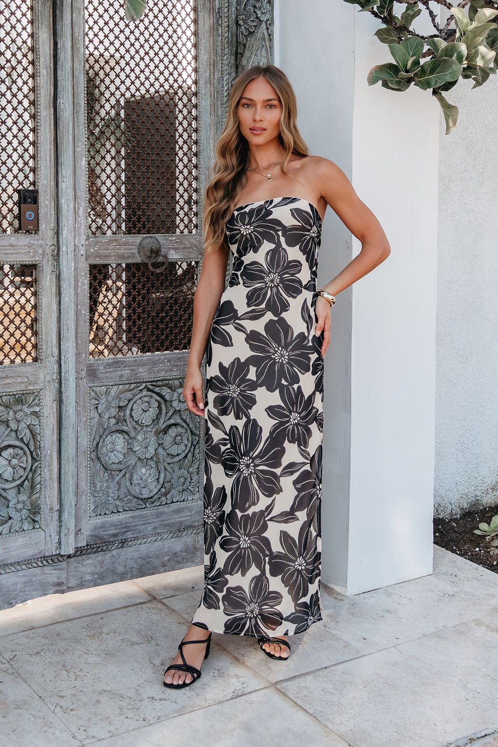 Woman wearing the Midnight Eclipse Strapless Maxi Dress, standing by an ornate wooden door outdoors.
