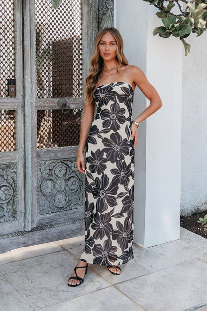 Woman wearing the Midnight Eclipse Strapless Maxi Dress, standing by an ornate wooden door outdoors.