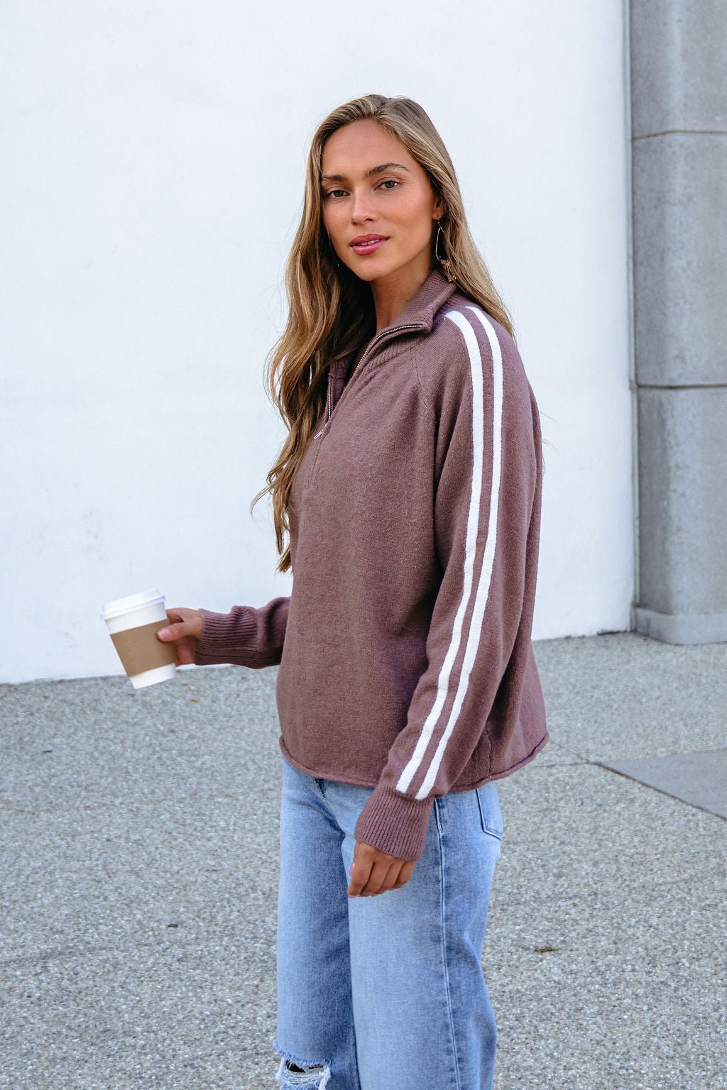 Woman in a Mocha Half Zip Collared Pullover holds a coffee cup while standing outside on a concrete surface.