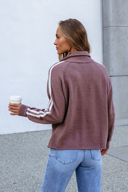 Woman with long hair in a Mocha Half Zip Collared Pullover and jeans holds coffee outdoors, facing away.