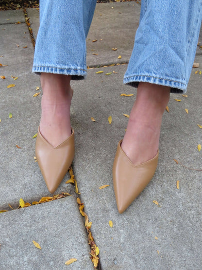 Standing on a stone pavement with yellow leaves, person wears light blue jeans and Morley Camel Open Back Kitten Heels.