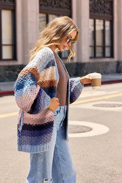 Woman in sunglasses wears a Multi Blue Stripe Crochet Cardigan and jeans, holding coffee while walking on a city street.