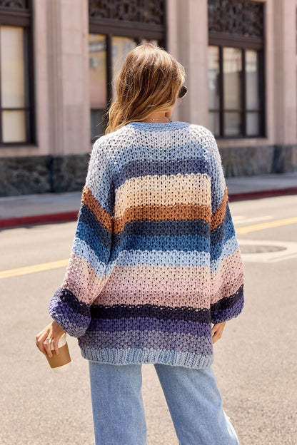 A person with long hair wearing a Multi Blue Stripe Crochet Cardigan holds a coffee cup while standing on a city street.