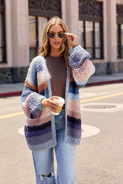 Woman in sunglasses wears the Multi Blue Stripe Crochet Cardigan, brown top, ripped jeans, holding coffee on a city street.