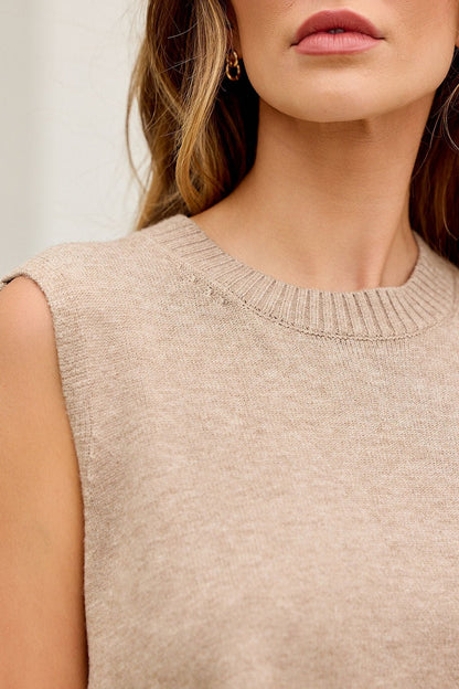 Woman in Nine To Five Cashmere Sweater, dark beige, sleeveless; loose hair, gold hoop earring; shown shoulders to lips.