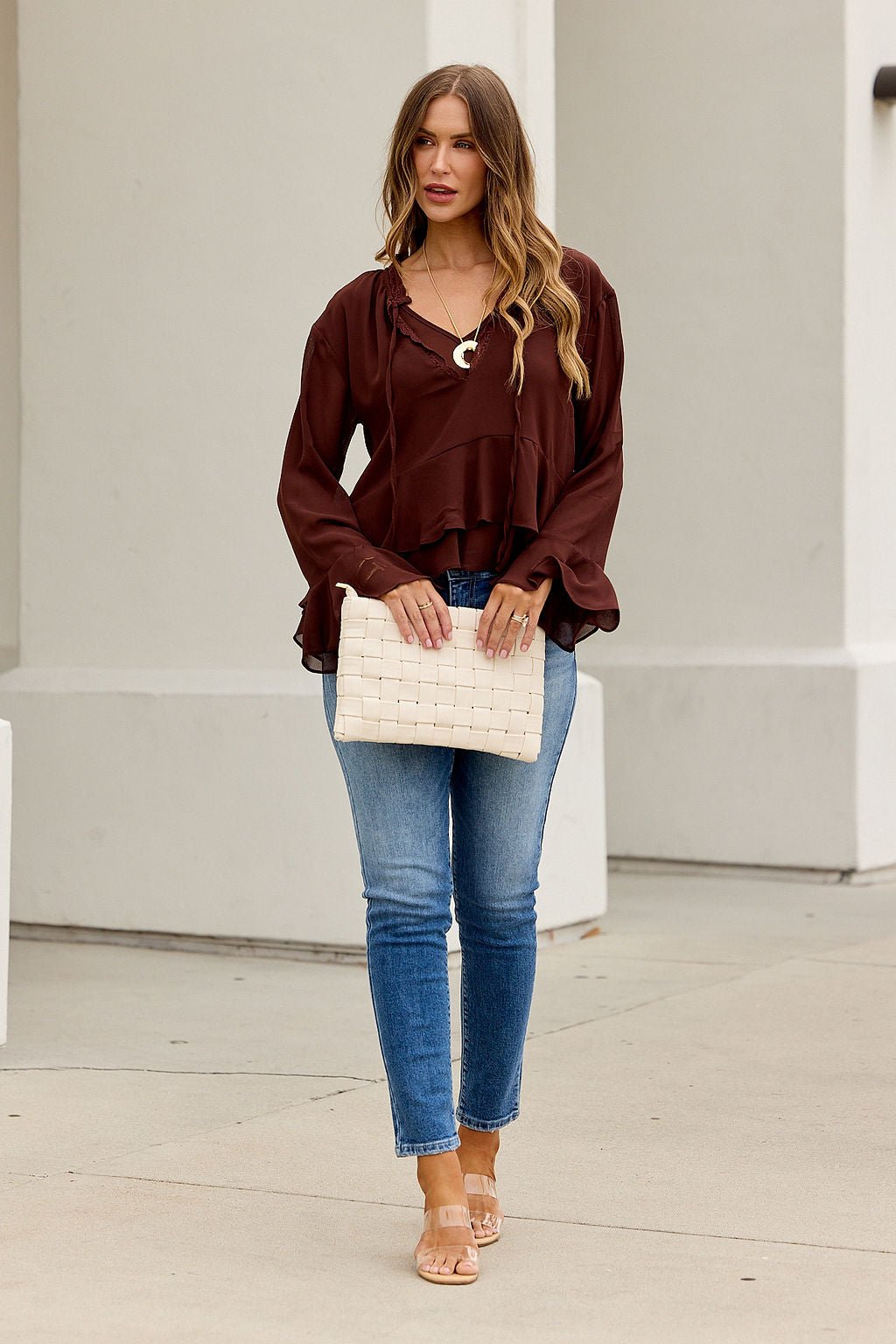 Woman in an Office Bell Sleeve Top - Brown holds a cream clutch—her look is perfect for work-to-weekend style.