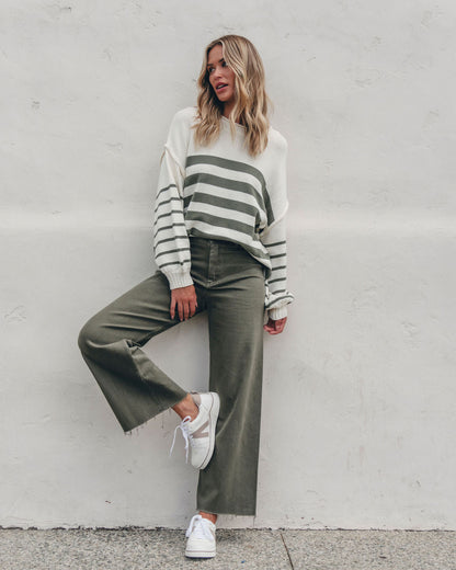 Woman wearing the Olive and Cream Striped Pullover Sweater leans against a white wall, showcasing a chic fall look.