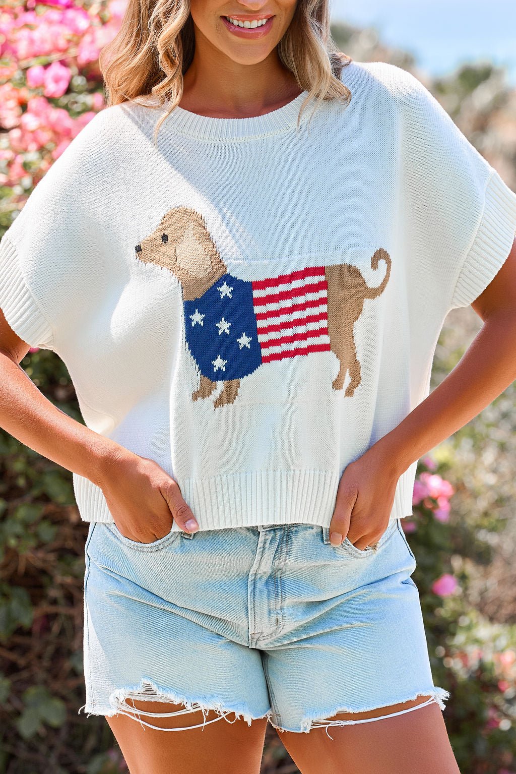 She wears the Patriotic Pup Knit Sweater - Cream with light denim shorts for a fun, casual look.