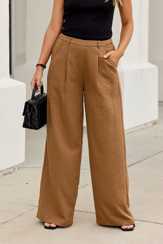 Woman in Power Pleated Wide Leg Pants - Camel, black top and sandals, holding a black handbag—versatile work-to-weekend style.