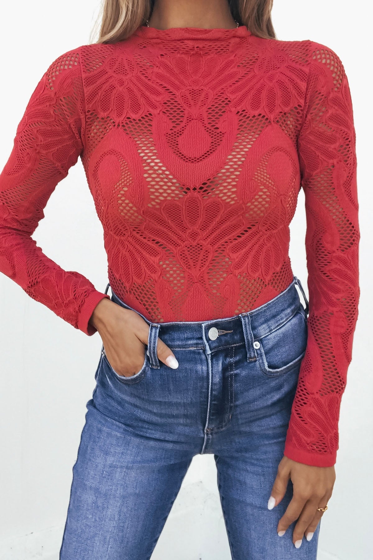 Woman in a Red Mock Neck Fishnet Top and high-waisted blue jeans, one hand tucked stylishly in her pocket.