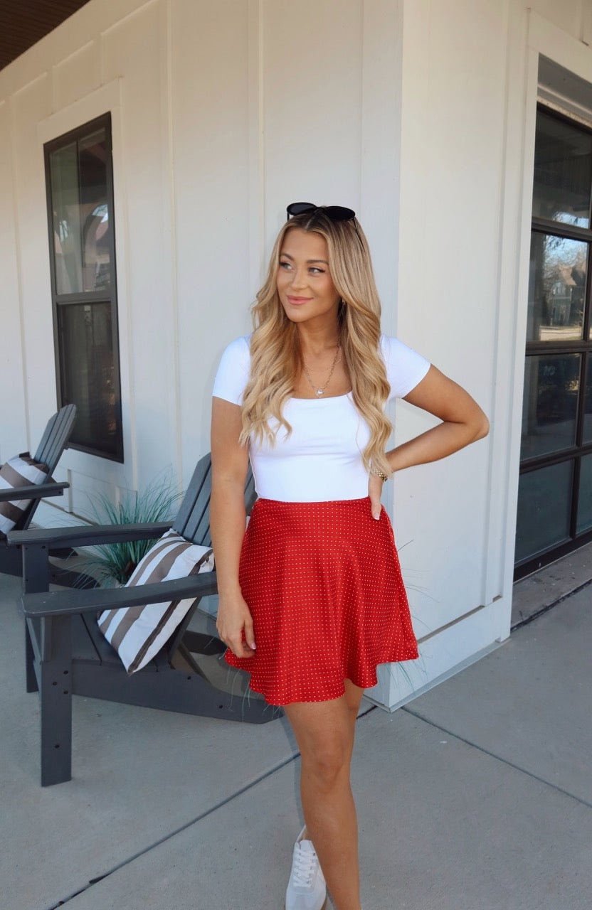 Woman smiles outdoors in a Red Polka Dot Satin Mini Skirt - FINAL SALE, paired with a white top.