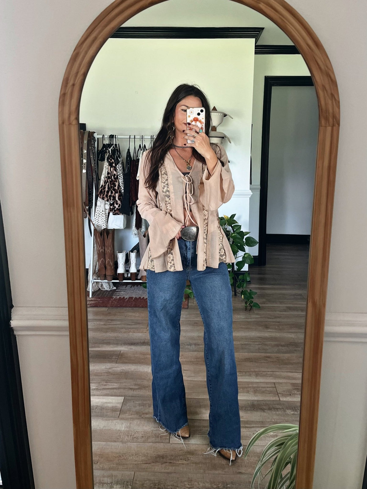 Woman takes a mirror selfie in boho room, wearing the Sand Bell Sleeve Sheer Lace Top-FINAL SALE under a beige jacket and layered necklaces.