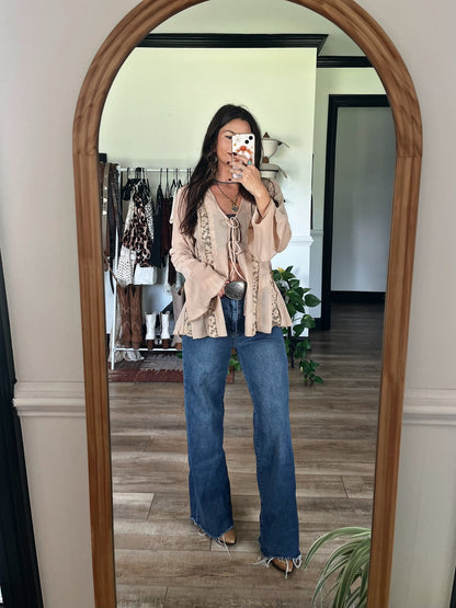 Woman takes a mirror selfie in boho room, wearing the Sand Bell Sleeve Sheer Lace Top-FINAL SALE under a beige jacket and layered necklaces.