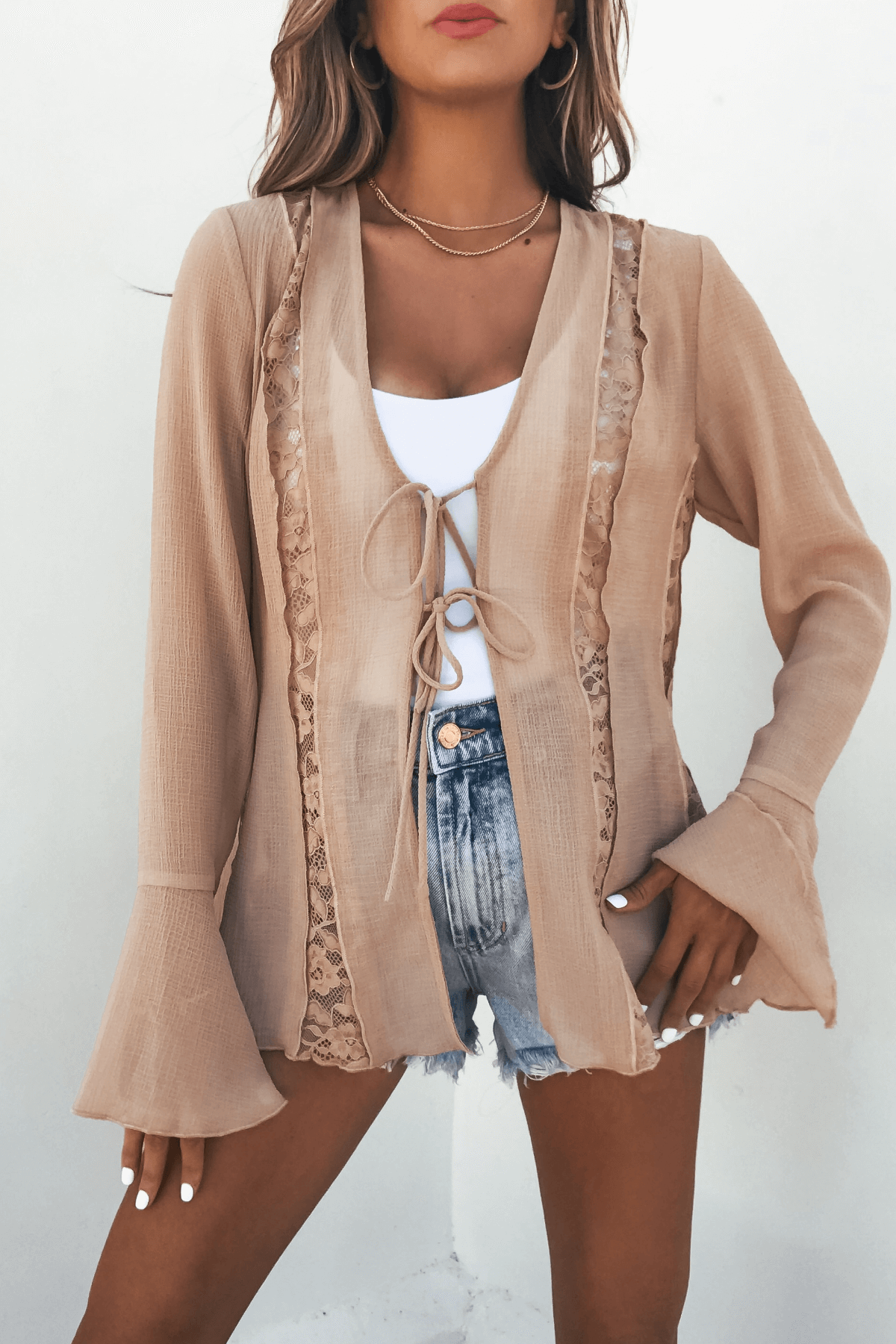 Woman modeling the Sand Bell Sleeve Sheer Lace Top over a white tank and denim shorts on a plain white background.