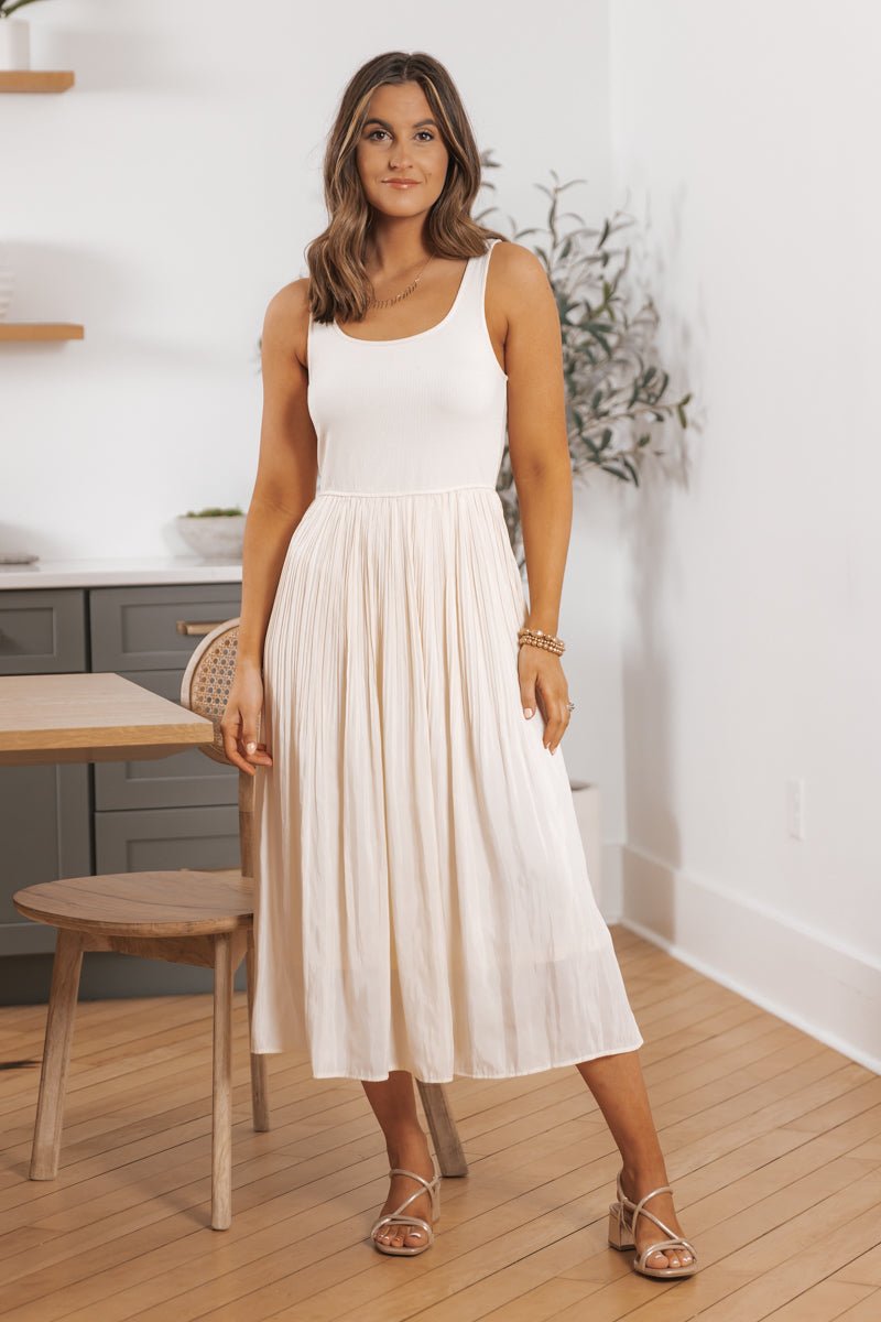 Woman in the Scoop Neck Pleated Skirt Midi Tank Dress stands indoors near a table and chair on a wooden floor.