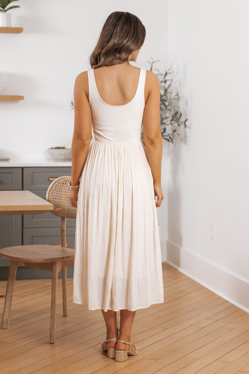 Woman in Scoop Neck Pleated Skirt Midi Tank Dress stands indoors on light wood floors, facing away amid minimal decor.