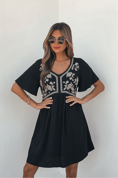 Woman in Seaside Embroidered Mini Dress - Black, sunglasses, and red lipstick stands against a plain white background.