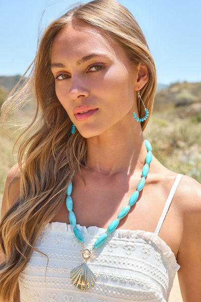 Woman with long blonde hair wears the Shell Charm Necklace - Turquoise - FINAL SALE with a white dress and coastal jewelry on a sunny day.