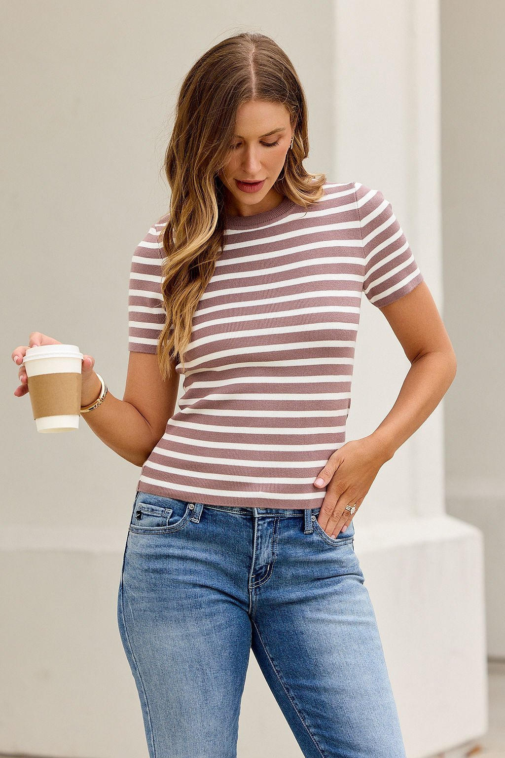Woman in a Short Sleeve Striped Sweater Tee - Mocha, holding a coffee cup outdoors against a light background.