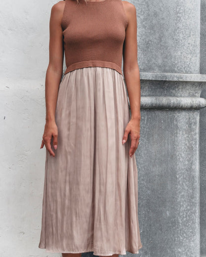 A woman in the Sleeveless Half Sweater and Satin Skirt Midi Dress - Mocha stands by a textured gray and white wall.