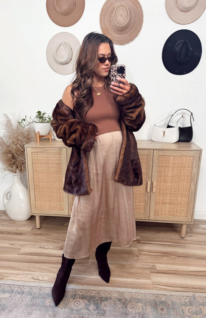 Woman in sunglasses and fur coat snaps a mirror selfie, wearing the Sleeveless Half Sweater and Satin Skirt Midi Dress in mocha.