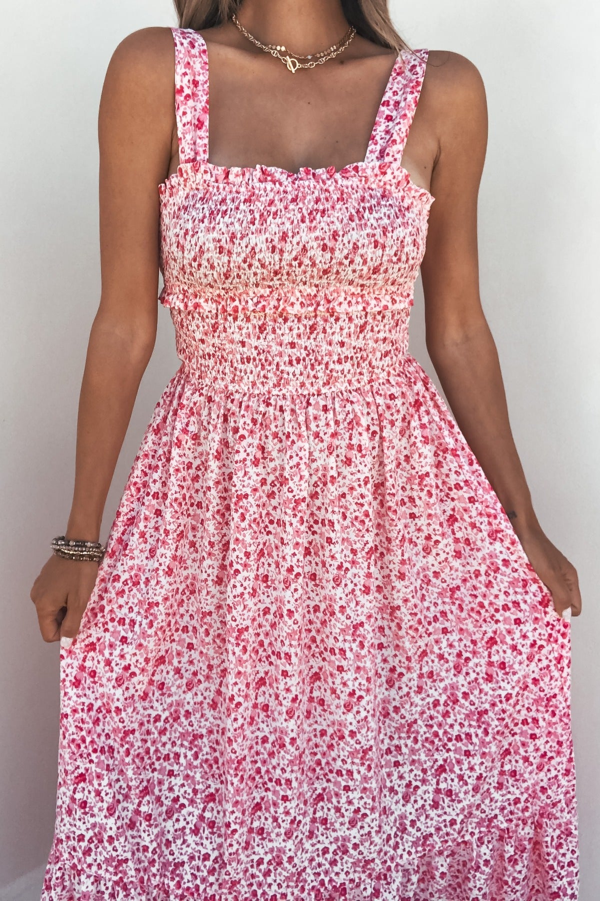 Woman in a Smocked Bow Tie Print Midi Dress - Pink, holding skirt sides against a plain background.