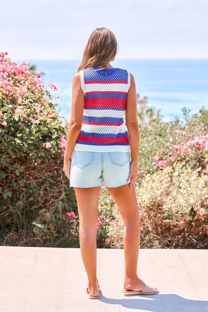 Woman in the Stars & Stripes Tie Front Sweater Vest stands on a coastal path, framed by blooming bushes.