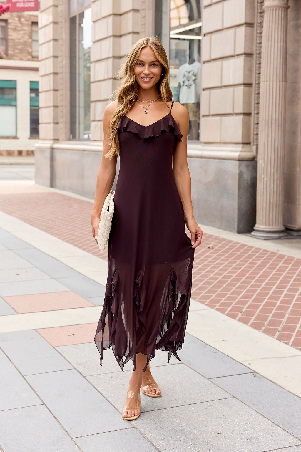 Woman wears the Steve Madden Mariane Midi Dress - Brow, Steve Madden sandals, and holds a white purse, smiling on a city sidewalk.