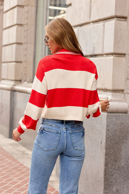 A person in blue jeans and a red striped button-up sweater walks on a city sidewalk, facing away from the camera.