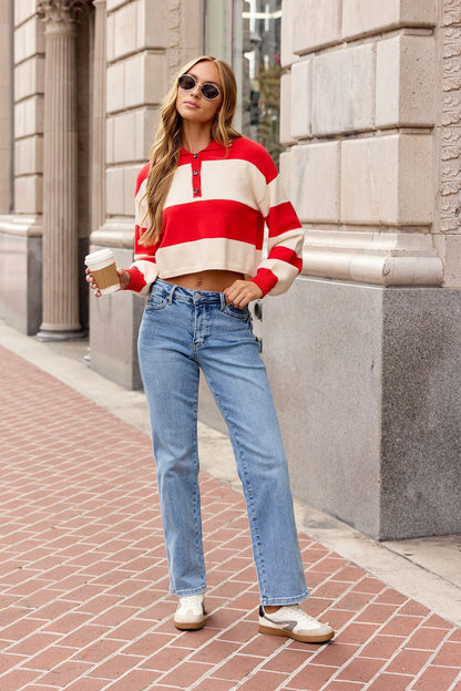 Woman in Striped Button Up Sweater - Red, blue jeans, and sunglasses holds coffee on city sidewalk.