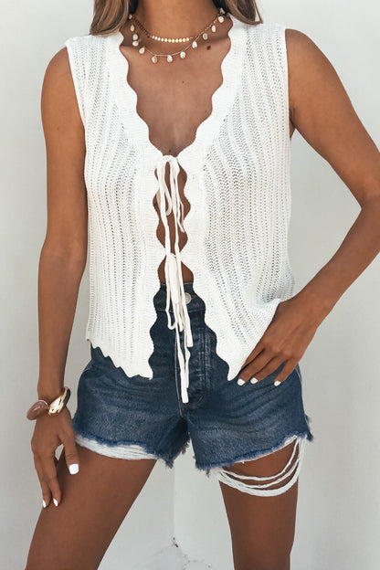 Woman wears a Sunlace Tie Front Sweater Vest in cream, distressed denim shorts, necklace, and bracelet against a white background.
