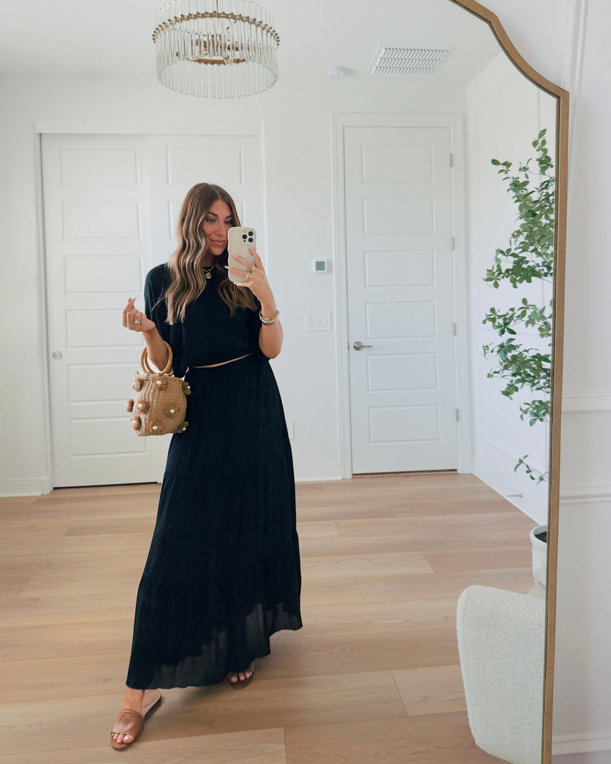 Woman in Sunrise Short Sleeve Top & Maxi Skirt Black Set takes a mirror selfie, holding a tan bag and wearing brown sandals.