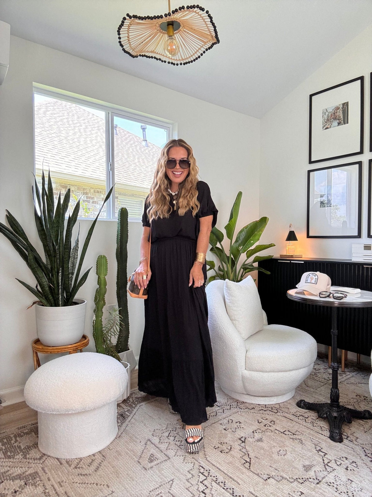 Woman wears the Sunrise Short Sleeve Top & Maxi Skirt Black Set in a bright, plant-filled room with white chairs and modern lighting.