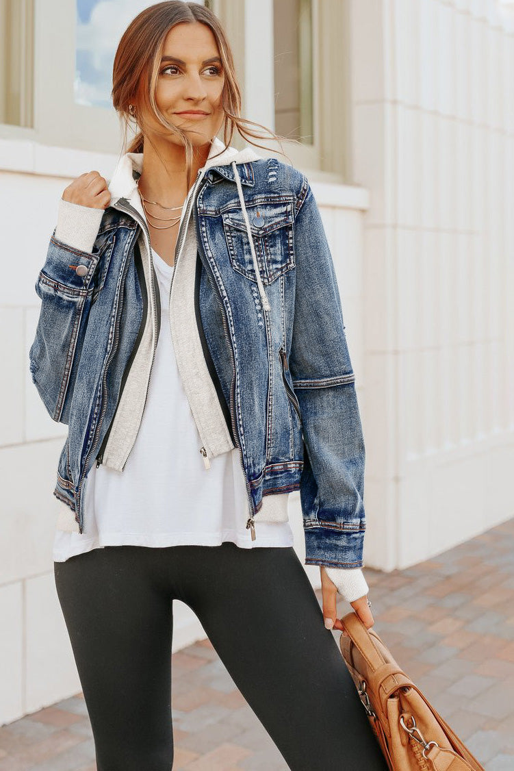 Woman in a Denim Jacket with Hoodie: Medium Wash, white shirt, black leggings, holding a brown bag on a paved sidewalk.