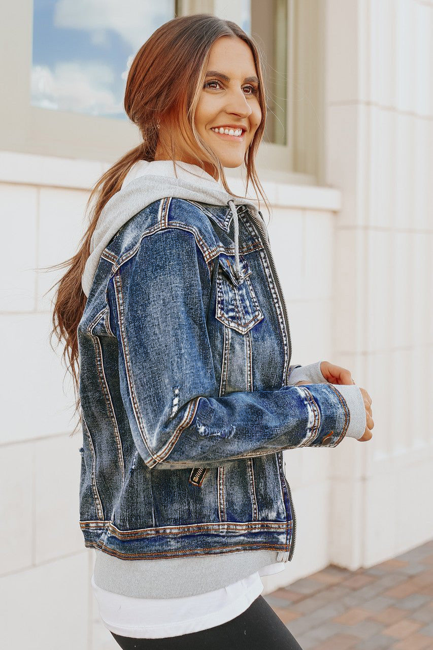 Woman smiles outdoors in the Denim Jacket with Hoodie: Medium Wash, showcasing versatile style by a light building.