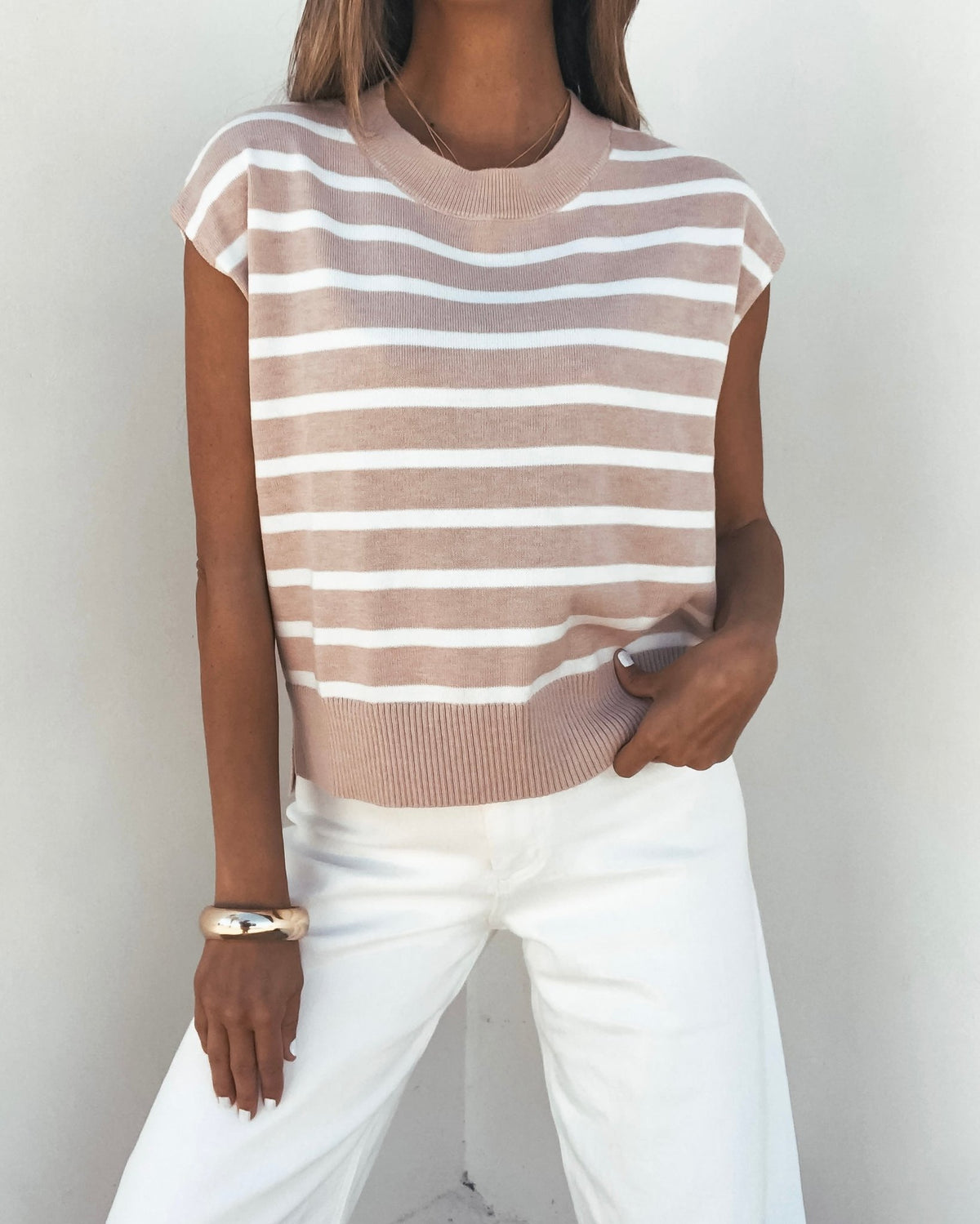 Woman models the Taupe Striped Cap Sleeve Sweater with white pants against a simple light background.